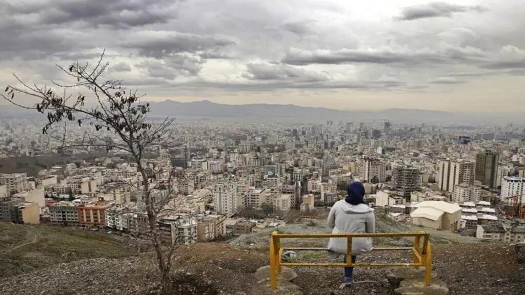 تصویری زنی نشسته روی نیمکتی در بام تهران